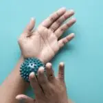 Close-up of hands using a spiky massage ball for therapy against a blue backdrop.